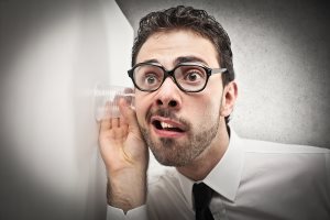 curious businessman listens with glass leaning against the wall
